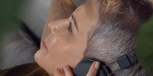 A woman lying back with headphones on, eyes open and relaxed.