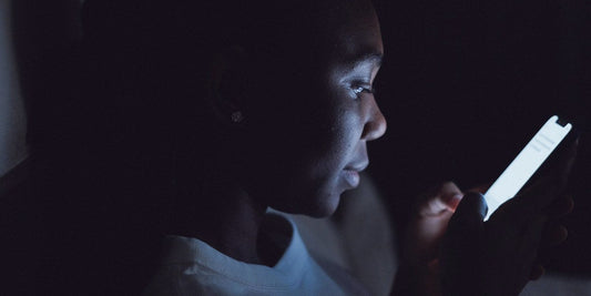 A woman awake in a dark room, her face lit only by the phone she is reading.