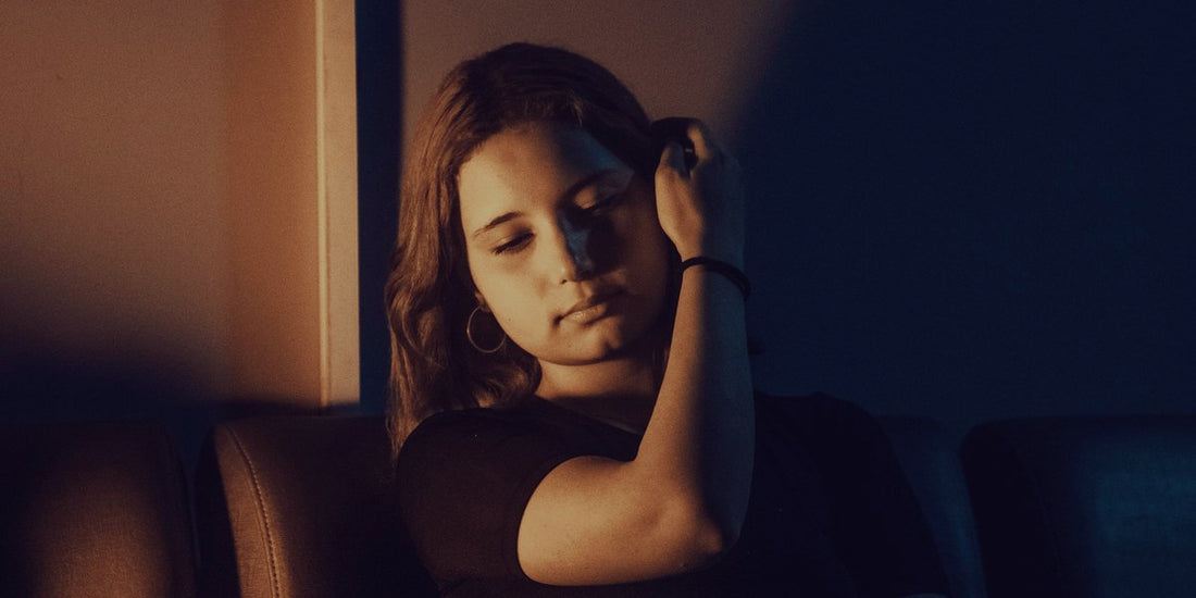 A woman sitting on a couch in the evening with her hand at her temple, still braced from the day.