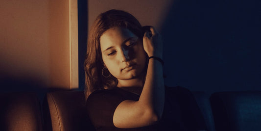 A woman sitting on a couch in the evening with her hand at her temple, still braced from the day.
