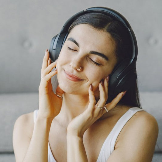 A woman with her eyes closed and a soft smile, hands resting on her headphones